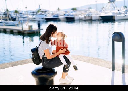 Madre sta baciando la sua bambina mentre si siede su un molo sul mare Foto Stock