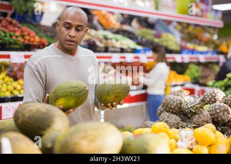 Uomo di mezza età che raccoglie il melone maturo al supermercato Foto Stock