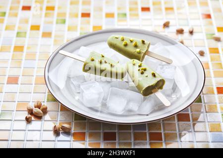 Pistacchio surgelato fatto in casa in ciotola di ghiaccio su tavola di tessere mosaico. Pop cicle rinfrescante, succo verde congelato sul bastone. Top vi Foto Stock