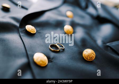 Due anelli di nozze d'oro su una giacca blu da uomo con bottoni con un'aquila a doppia testa. Foto Stock