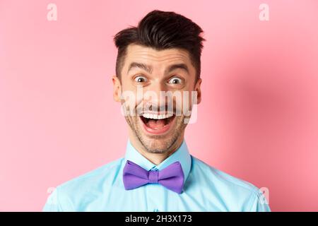 Primo piano di ragazzo giovane sorpreso e felice, bocca aperta e sorridente stupito, dando un'occhiata all'offerta promozionale, in piedi in bow-tie sopra pin Foto Stock