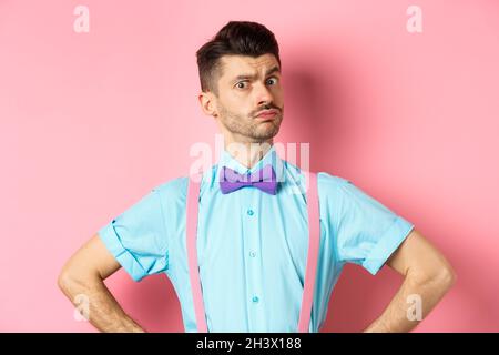 Immagine del giovane uomo con baffi divertenti e bow-tie in piedi in posizione sicura, fissando con incredulità e dubbi a macchina fotografica, pos Foto Stock