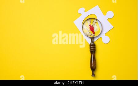 Gli uomini piccoli di legno si trovano e una lente di ingrandimento di legno su uno sfondo giallo. Concetto di ricerca di persone di talento e uniche Foto Stock