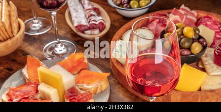 Panorama gourmet di antipasti di vino con un bicchiere di vino rosato, un tagliere di formaggio Foto Stock