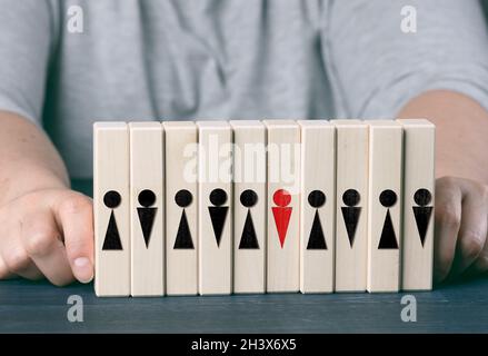 Due mani femminili tengono i cubetti di legno con i piccoli uomini su un tavolo blu. Concetto di cura del team, scelta del leader, coesione del team Foto Stock