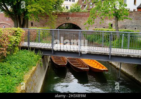 Una vista panoramica di un piccolo ponte, barche di legno (Ulmer Schachteln) sotto di esso, alberi verdi e le mura della città vecchia nella città di Ulm in Germania Foto Stock