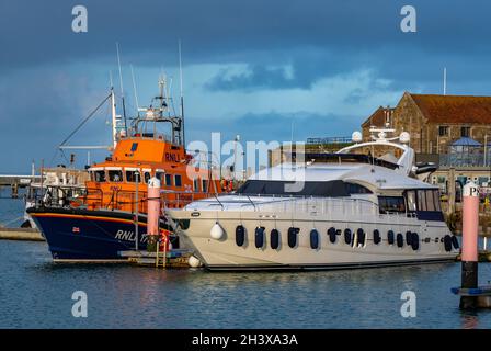 La scialuppa di salvataggio di RNLI margaret joan e fred Nye per tutte le condizioni meteorologiche severn Class scialuppa di salvataggio nel porto di yarmouth sull'isola di wight ormeggiata accanto a una barca a motore di lusso. Foto Stock