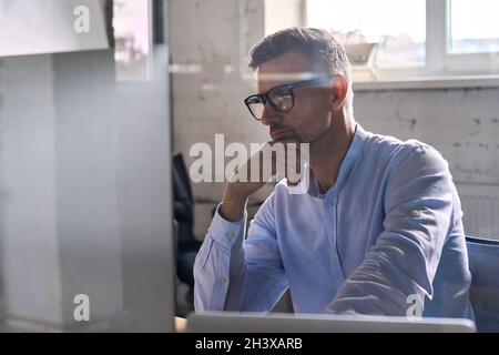 Uomo d'affari attento che lavora usando il calcolatore nell'ufficio moderno al tavolo. Foto Stock