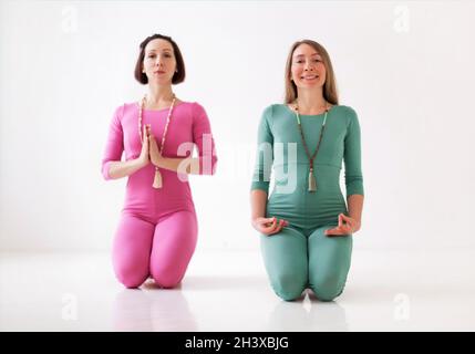 Due giovani donne in lunghe tute sportive che si esibiscono in asana yoga insieme in studio Foto Stock