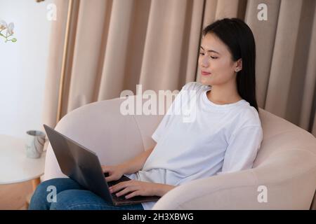 Ritratto di donna asiatica godendo utilizzando il computer portatile in appartamento interno soggiorno interno. Concetto di streaming del webinar sulle videochiamate. Foto Stock