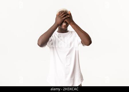 Ritratto di felice afro-americano giovane ragazzo, occhi stretti e sorridente divertito, in attesa di sorpresa, in piedi su sfondo bianco Foto Stock