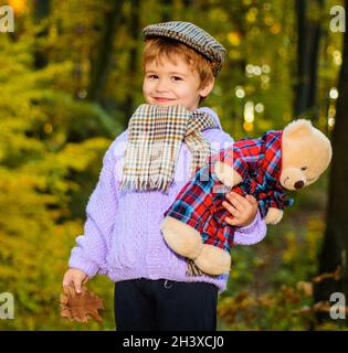 Autunno ragazzo. Bellissimo bambino in caldo maglione. Ragazzino che gioca con orsacchiotto nel parco autunnale. Foto Stock