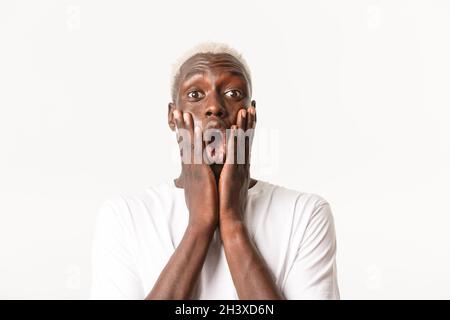 Primo piano di impressionato e stupito bell'uomo biondo afroamericano, mascella goccia e dicendo WOW stupito, tenendo le mani sul volto, Foto Stock