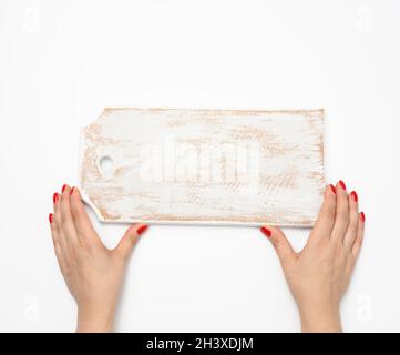 La mano femmina con manicure rosso contiene il tagliere rettangolare vuoto in legno da cucina su sfondo bianco Foto Stock