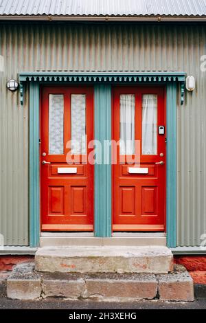 Due porte d'ingresso arancioni con vetro e tende in una porta blu. Foto Stock