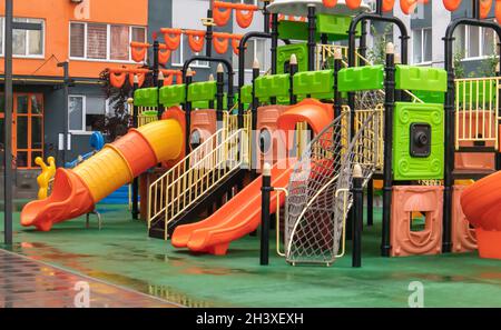 Un cortile di alti edifici con un nuovo moderno e colorato e grande parco giochi in una piovosa giornata estiva senza persone. O vuoto Foto Stock