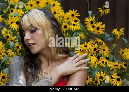 Un grazioso modello Brunette si pone in Un campo di fiori gialli mentre si gode il tempo estivo Foto Stock