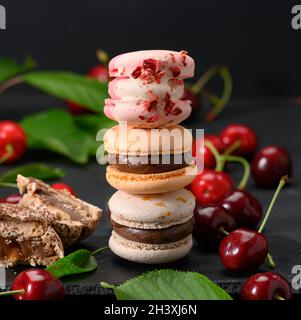 Pila di macaron multicolore e ciliegie rosse mature su sfondo di legno nero Foto Stock