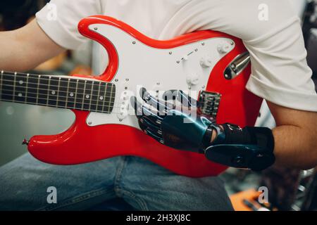 Il giovane uomo disabile con protesi artificiale suona la chitarra in negozio. Foto Stock