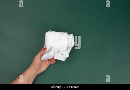 La mano di una donna tiene uno straccio bianco sullo sfondo di una tavola di gesso verde Foto Stock