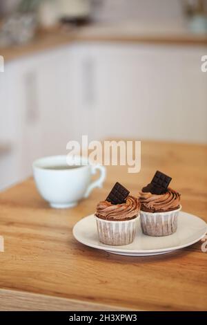 Due muffin su piatto bianco decorati con crema di cacao e pezzi di cioccolato con una tazza di tè Foto Stock
