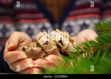 Primo piano le mani femminili con tre piccoli regali artigianali. Giovane donna hipster in maglione di Natale che tiene 3 regali organici, arco di corda. Accogliente inverno caldo de Foto Stock