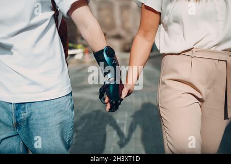 Giovane uomo disabile con mano protesica artificiale che cammina e tiene la mano della ragazza della donna. Foto Stock