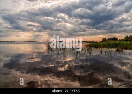 Un tramonto colorato e un'espressiva riflessione del cielo in un lago tranquillo e tranquillo con canne in primo piano Foto Stock