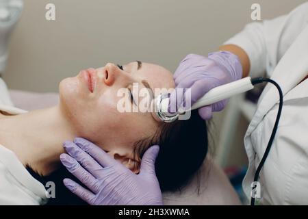 Primo piano della donna di testa che riceve la terapia facciale di phonoforesis di elettroporazione al salone di bellezza di centro termale. Foto Stock