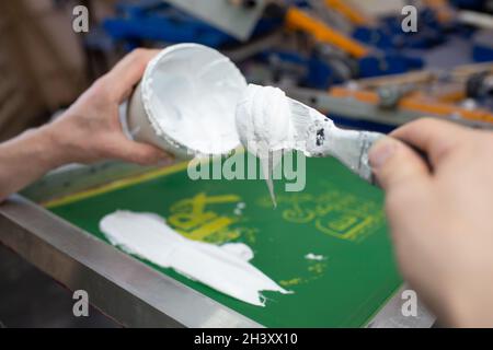 Serigrafia serigrafica processo di stampa presso la fabbrica di abbigliamento. Applicazione di vernice su vernici a colori di telaio, spatola e plastisol Foto Stock
