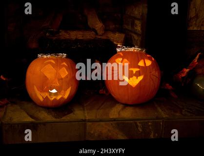 Due zucche di Halloween intagliate a casa, una con un disegno del gatto. Illuminato Jack o Lanterne all'interno della casa per Halloween. Foto Stock