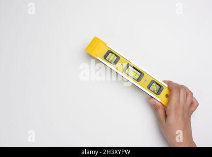 La mano femmina tiene un livello di plastica giallo su uno sfondo bianco Foto Stock