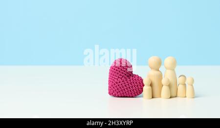 Il cuore a maglia rossa e la famiglia di figurine in legno su sfondo blu. Il concetto di coesione e di amore nella famiglia, l'amore per chi Foto Stock