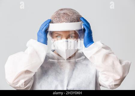 Operatori medici, covid-19 pandemia, concetto di coronavirus. Primo piano sorridente medico donna fiducioso messo su equipaggiamento protettivo personale Foto Stock