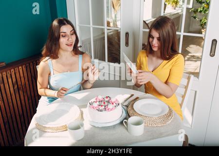 Donne felici amici a casa seduta e sorridente di bianco torta di compleanno Foto Stock