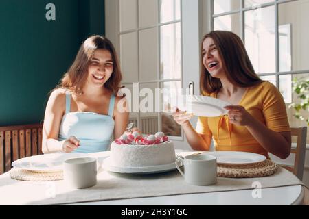 Donne felici amici a casa seduta e sorridente di bianco torta di compleanno Foto Stock