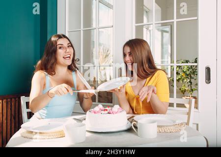 Donne felici amici a casa seduta e sorridente di bianco torta di compleanno Foto Stock