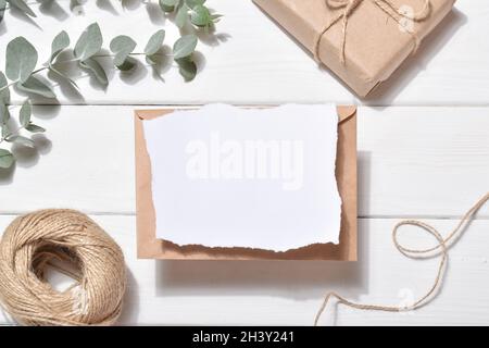 Un invito vuoto su sfondo bianco con rami di eucalipto e filo naturale. Romanticismo. Layout piatto, vista dall'alto, posizione da copiare. Foto Stock