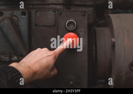 La mano dell'operaio preme con il dito il pulsante rosso sul vecchio sistema di apparecchiature industriali. Foto Stock