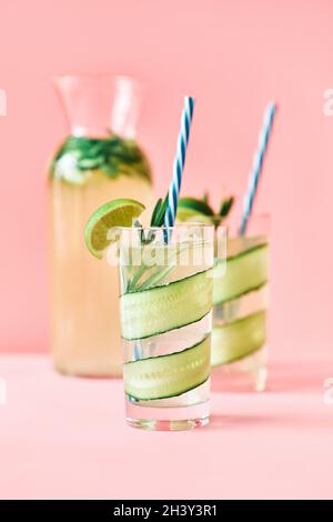 Cocktail rinfrescante con calce, cetrioli, rosmarino e ghiaccio in bicchiere su sfondo rosa Foto Stock