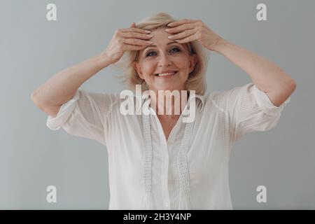 Anziano caucasico vecchio anziano donna grigio capelli ritratto facendo Facebuilding yoga viso ginnastica yoga auto massaggio. Foto Stock