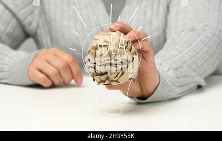 La mano femmina contiene una sfera di carta bruna grattata. Nuova idea, brainstorming Foto Stock