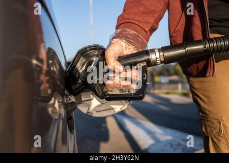 Primo piano a disposizione di un uomo caucasico sconosciuto tenere l'ugello nero della pompa del gas versando benzina nel serbatoio del carburante rifornimento di petrolio al veicolo in modalità self-service Foto Stock