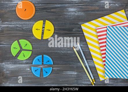 Frazioni multicolore, blocchi, taccuino su un tavolo di legno grigio. Ritorno a scuola, matematica divertente, giochi per l'asilo, istruzione prescolare. Foto Stock