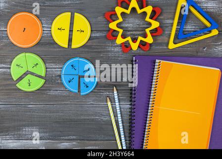 Frazioni multicolore, blocchi, taccuino su un tavolo di legno grigio. Ritorno a scuola, matematica divertente, giochi per l'asilo, istruzione prescolare. Foto Stock