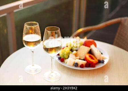 Tagli di formaggio assortiti e piatto di frutta da due bicchieri di vino bianco Foto Stock