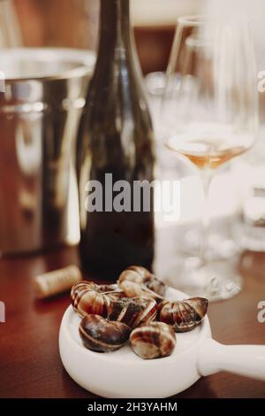 Escargots su teglia di ceramica bianca accanto al vino bianco Foto Stock