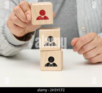 La mano femmina tiene un cubo di legno con un uomo. Il concetto di trovare una gerarchia di leader, un dipendente di talento, all'interno del team Foto Stock