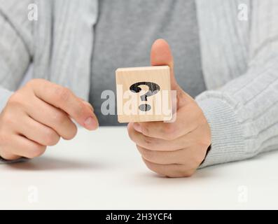 Mano femmina che tiene un cubo di legno con un punto interrogativo, concetto di risposte e domande, suspense e metodi di soluzione Foto Stock