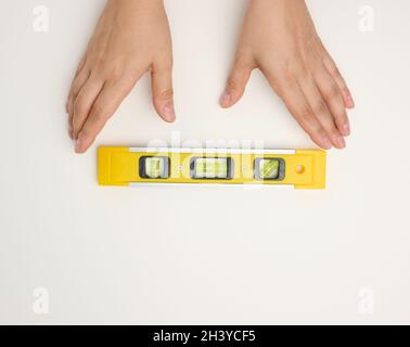 Le mani femminili reggono un edificio giallo in plastica su sfondo bianco Foto Stock